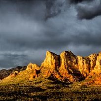 Sedona Splendor Courthouse Butte, Lee Mountain, Gibraltar Rock and Twin Buttes along Route 179 brightly lit at sunset under dark stormy skies in Sedona, AZ