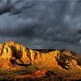 Sedona Splendor Courthouse Butte, Lee Mountain, Gibraltar Rock and Twin Buttes along Route 179 brightly lit at sunset under dark stormy skies in Sedona, AZ